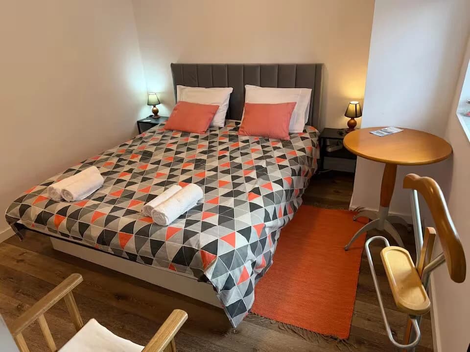 Schlafzimmer mit Doppelbett, Dekokissen und kleinem Tisch am Fenster