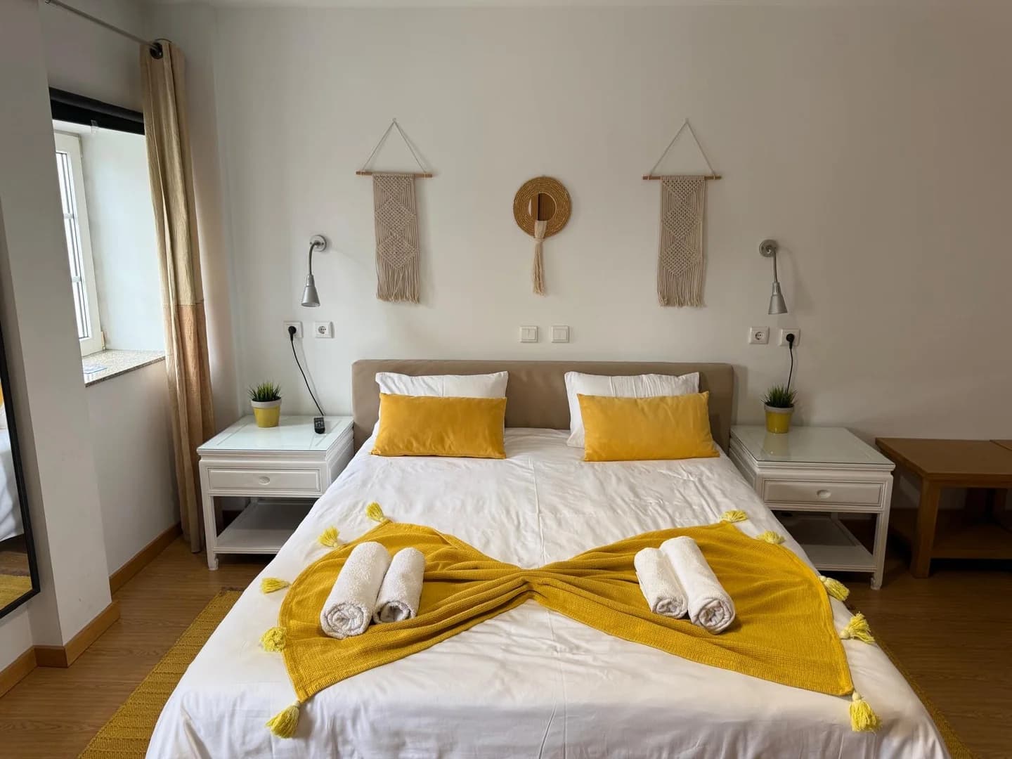 Quarto acolhedor com cama de casal, roupa de cama branca e detalhes em amarelo, decoração minimalista e ambiente luminoso.
